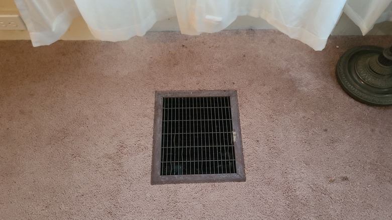 An old floor vent surrounded by pink carpet