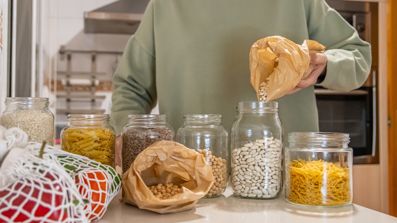 A person pouring dry goods into glass storage containers