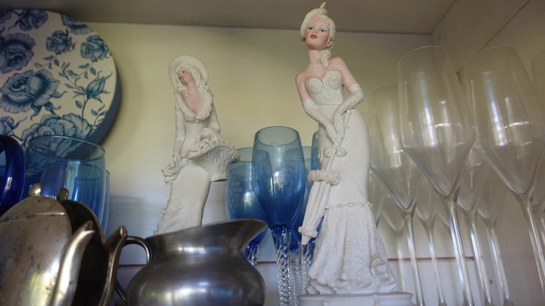Various crockery in a flea market Porcelain dolls Champagne flutes Pewter pots
