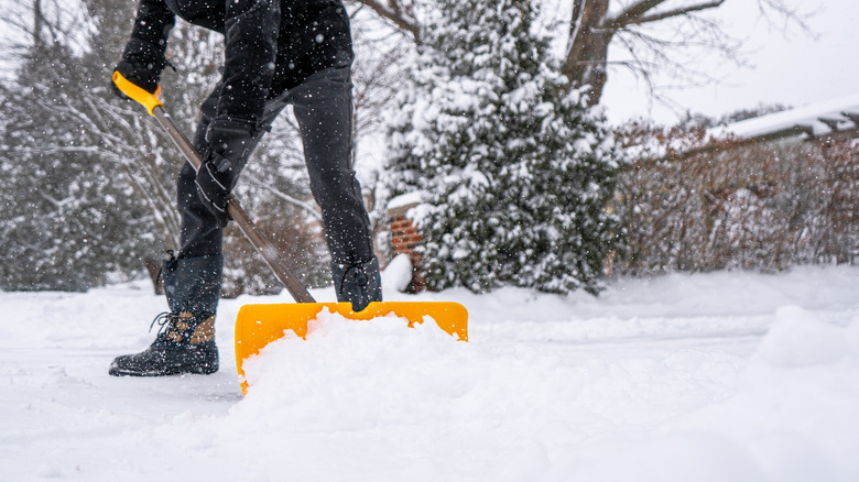 Man clearing snow from driveway with a yellow snow shovel