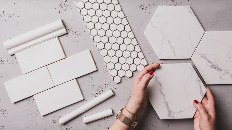 Hands holding bathroom tile with different shaped tiles laying across counter.