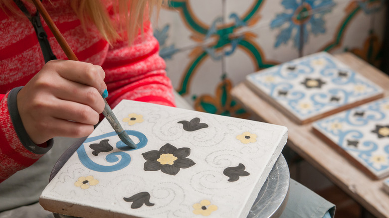 A pottery decorator painting a ceramic tile with floral motifs.