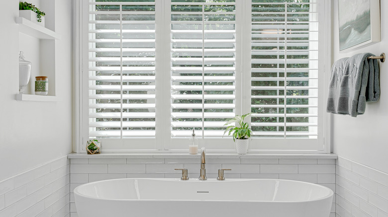 Modern luxury soaking tub with brass faucet interior design staged with plantation shutters.