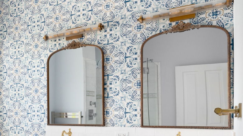 Bathroom vanity with two bronze mirrors and a blue and white geometric wallpaper
