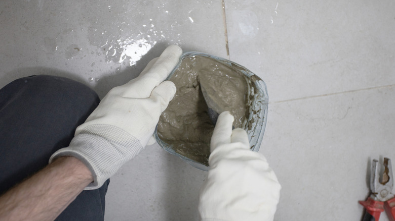 Wet cement mortar is being mixed in a bathroom with white tile floors.