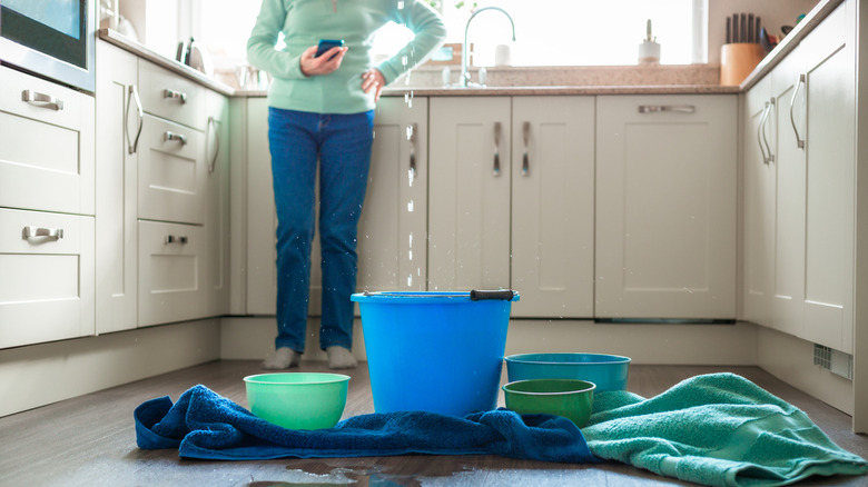 A person in a kitchen with buckets and towels on the floor to catch water dripping from the ceiling