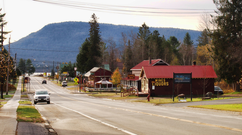 Road with cars through a small downtown with a few buildings and a sidewalk, mountain in background