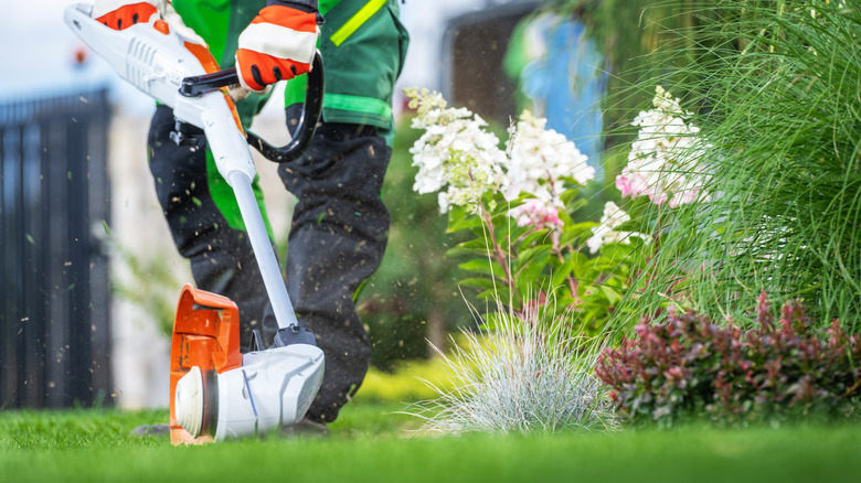 A close up of someone's gloved hands and legs while they're trimming a yard with a white and orange lawn trimmer.