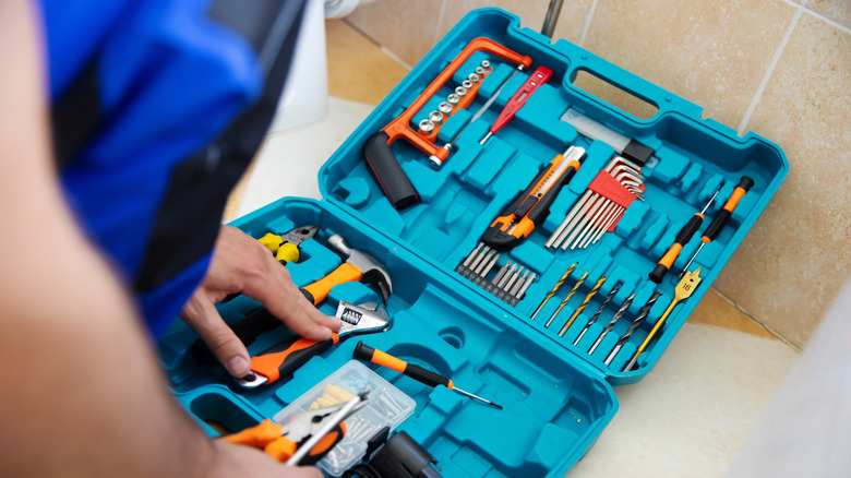 Blue tool kit on bathroom floor with various tools and drill bits.
