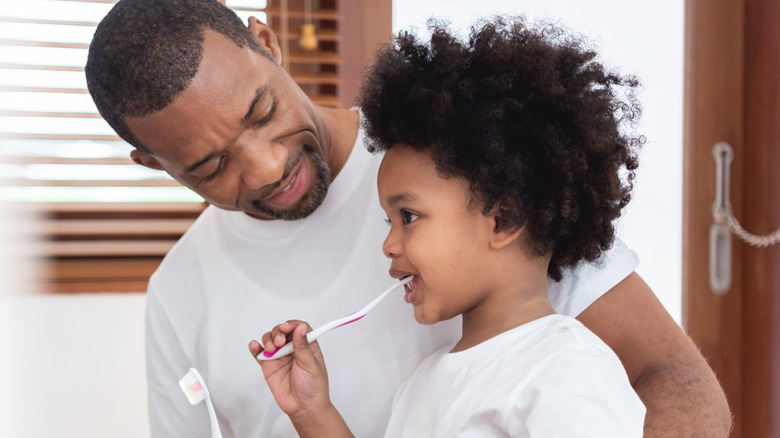 dad helping child brush teeth