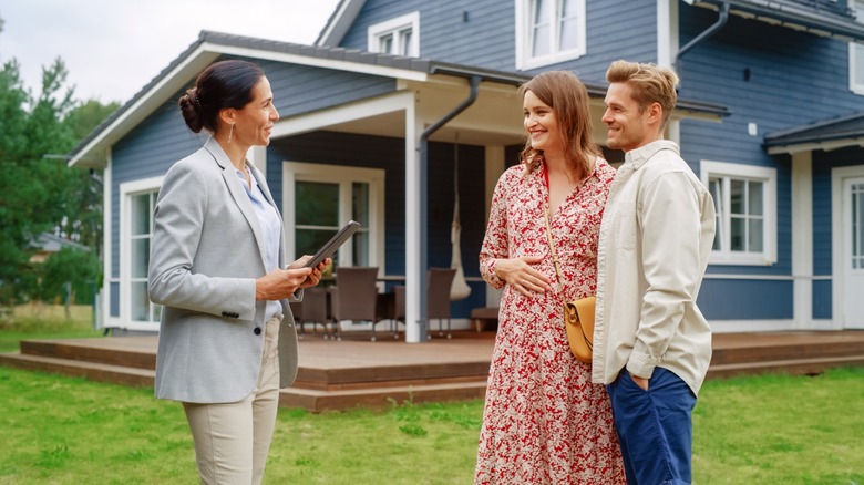 Young couple meeting real estate agent outside country home for sale.