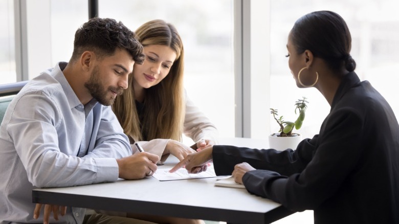 Real estate agent helping young couple fill out paperwork for home sale