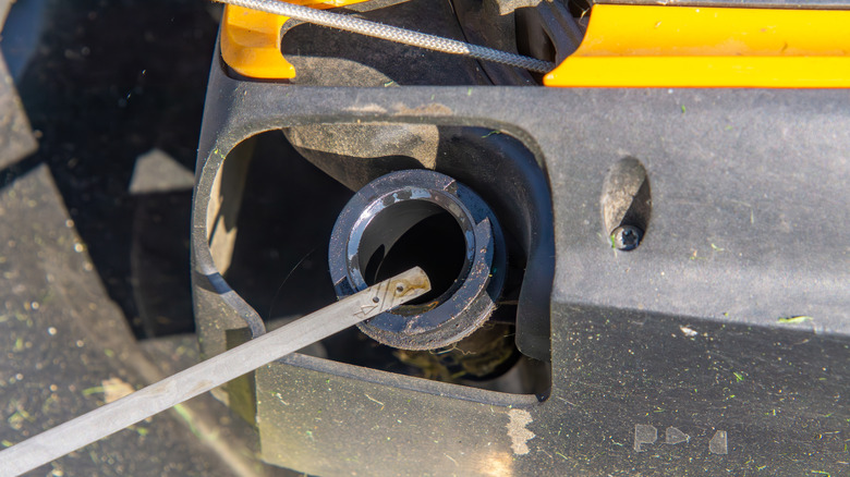 Holding dipstick over a lawn mower