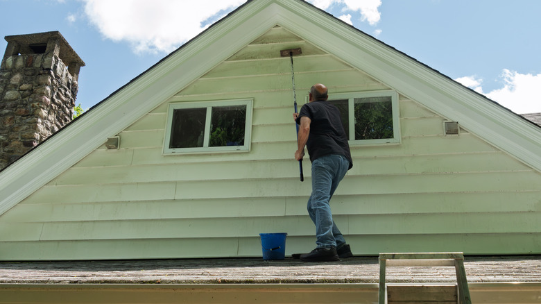 man standing on roof cleaning siding under gable of home