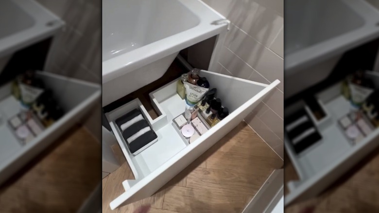 A mirrored image of a storage cabinet under the tub with items neatly stacked inside