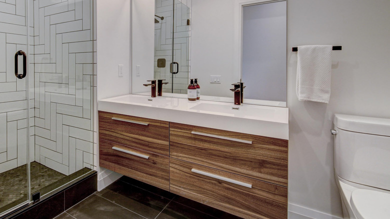 A contemporary bathroom featuring a wooden vanity with sleek drawers and a large mirror