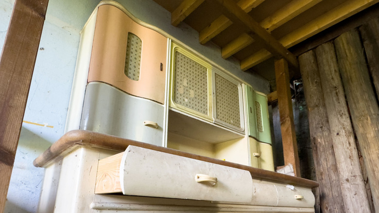 A vintage kitchen cupboard with wavy lines, two drawers, and a wooden counter in painted pastel colors.