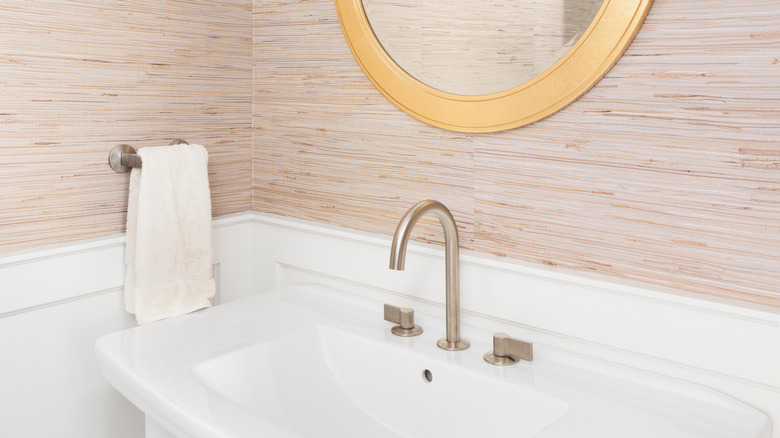 A bathroom vanity surrounded by textured wallpaper and wainscoting on the walls