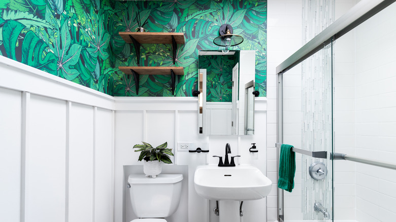 A white bathroom with green floral wallpaper and wainscoting
