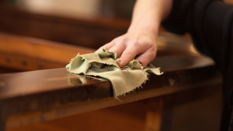 A hand wipes down a piece of wood furniture with a cloth.