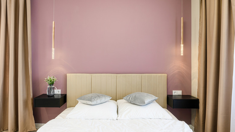 A bedroom with a mauve accent wall, hanging lights, and tan curtains.