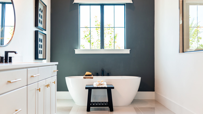 Modern bathroom with white cabinets, white bathtub and black accent wall