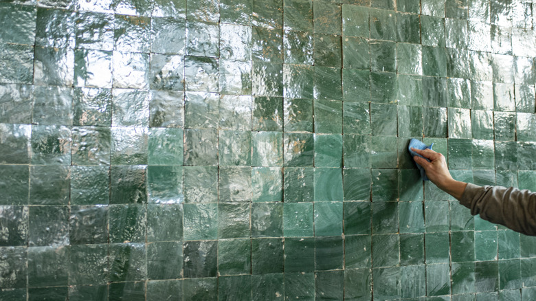 a person's hand cleaning a green zellige tile wall