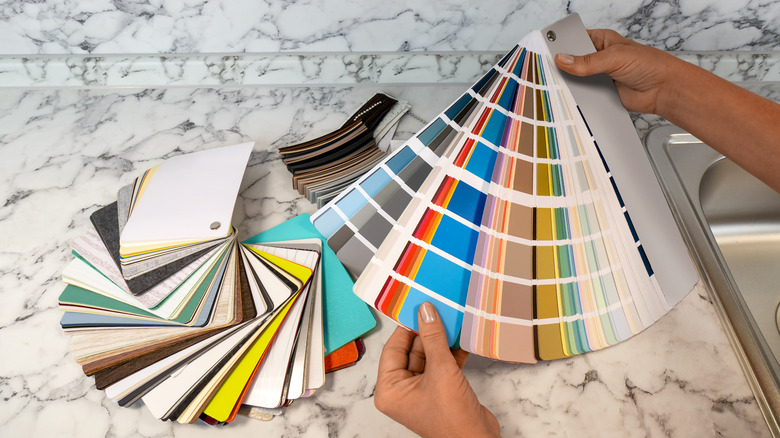 A closeup of a person holding color swatches on a kitchen countertop