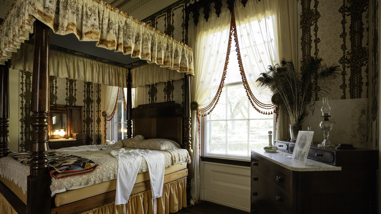 Traditional wooden canopy bed featuring ornate patterns, heavy drapery, and dark colors