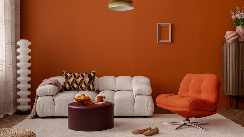 Warm modern living room with burnt orange walls, soft white sofa, and retro swivel chair.