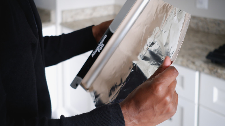 Close up of a person unrolling aluminum foil from the box