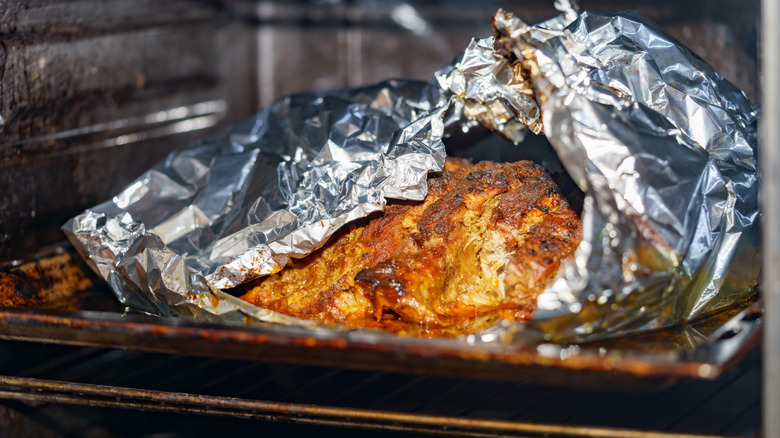 Meat partially wrapped in aluminum foil inside an oven