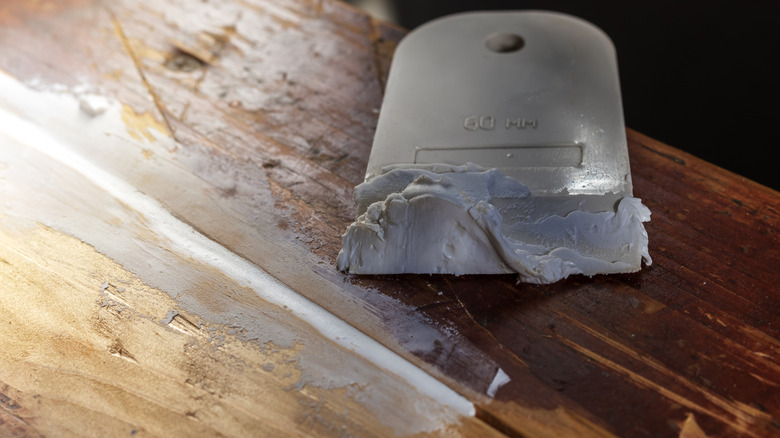 A putty knife with wood filler on it sits next to a crack that's being filled
