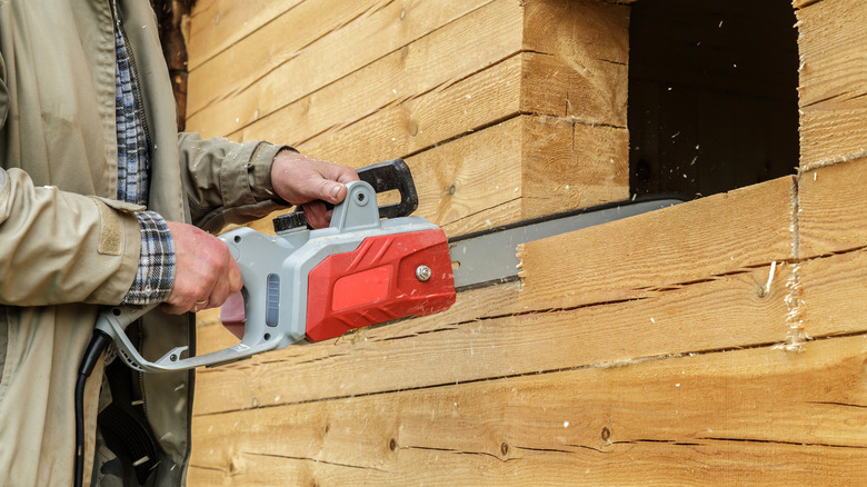 Person using a chainsaw to cut a window in a wooden wall