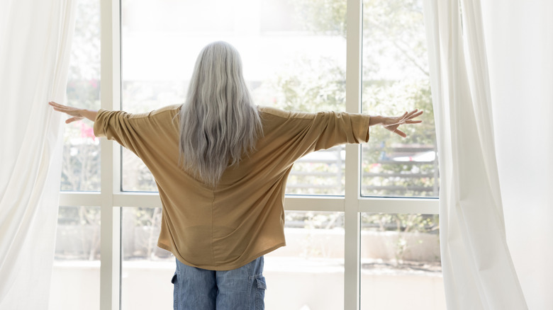 Woman staring out of a window with the drapes open.