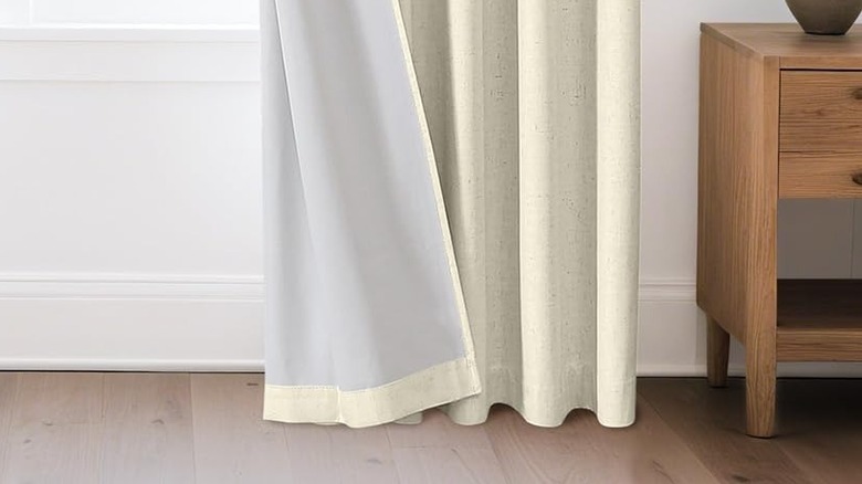White drapes with a white plastic backing hang in front of a window in a bedroom.