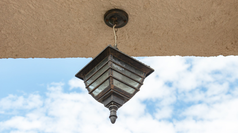 A dirty glass pendant light with a metal frame hanging outside
