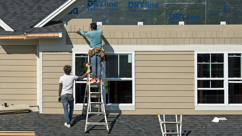 contractors installing beige siding on a house exterior