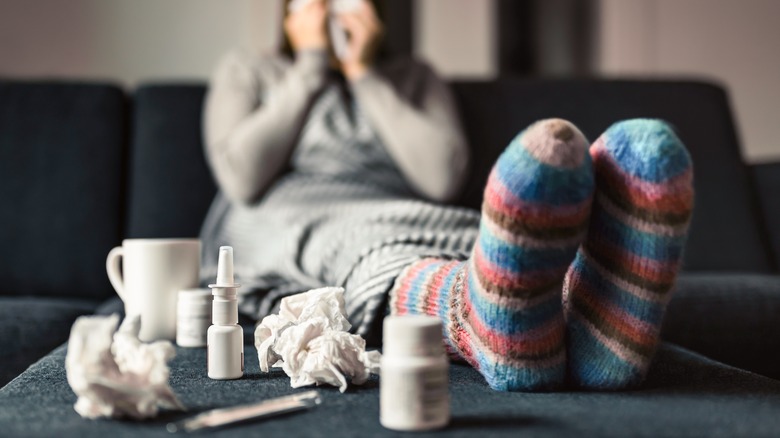 a Person sneezing with a bunch of pills in front on home couch.