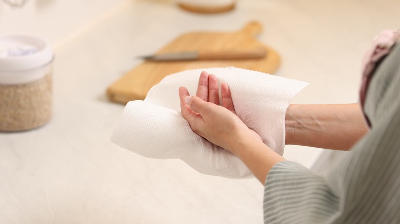 a woman wiping hands with paper towel in kitchen