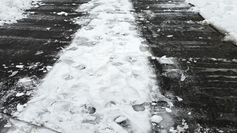 Dark-colored asphalt driveway partially covered in snow