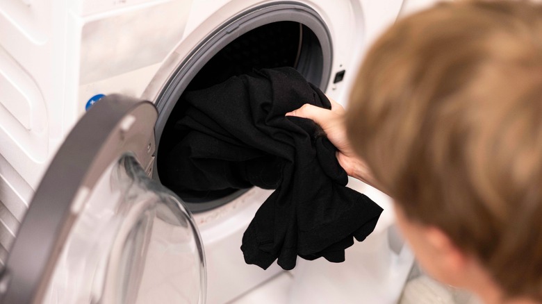 person putting dark black clothes in white washer