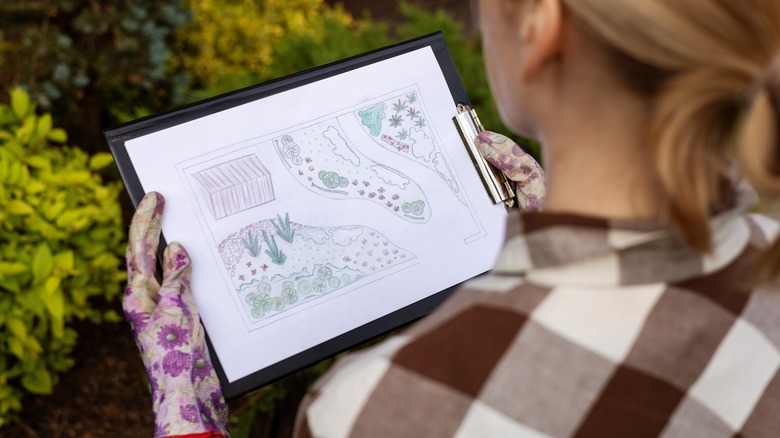 gardener looking at home backyard garden plan on paper attached to clipboard