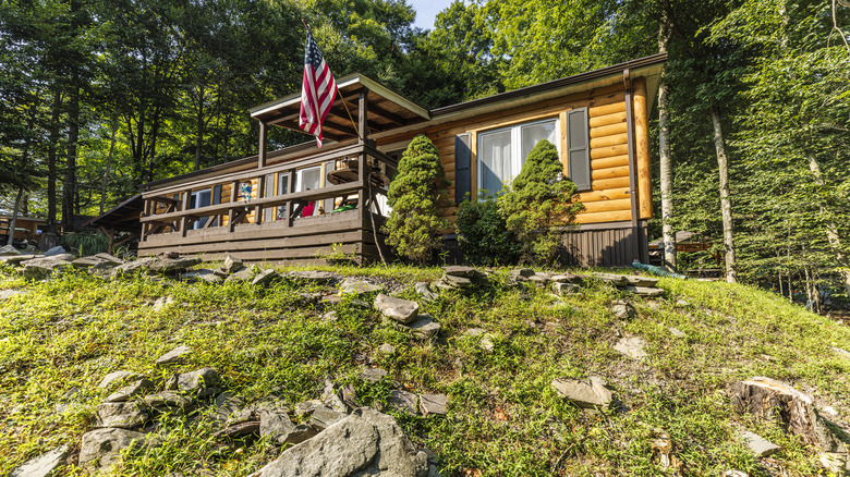 A prefabricated log cabin sits on rocky terrain deep in the woods