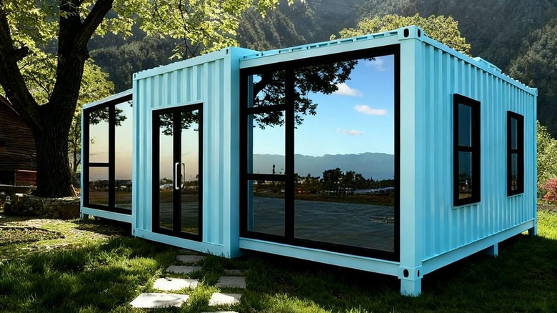 A modern sky blue modular prefab home is surrounded by trees