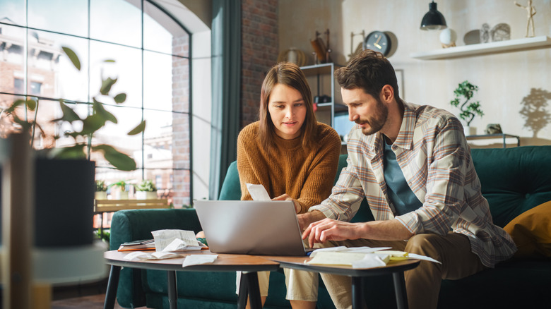 A couple sits together on a sofa while calculating their taxes