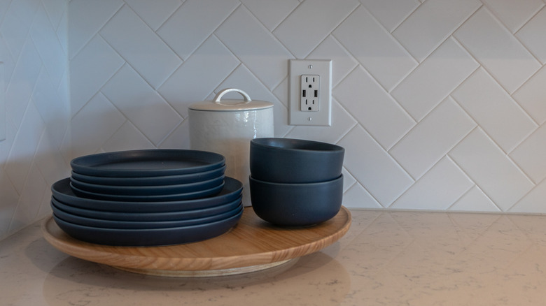 A lazy Susan on a countertop holding dishes and a ceramic jar