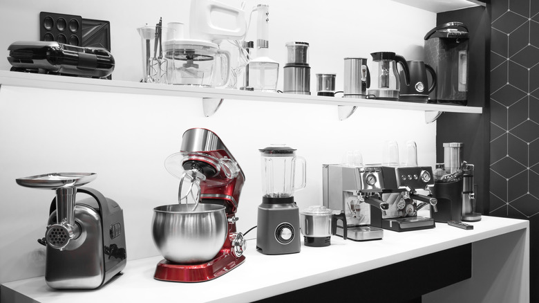 Two white shelves full of a variety of small kitchen appliances