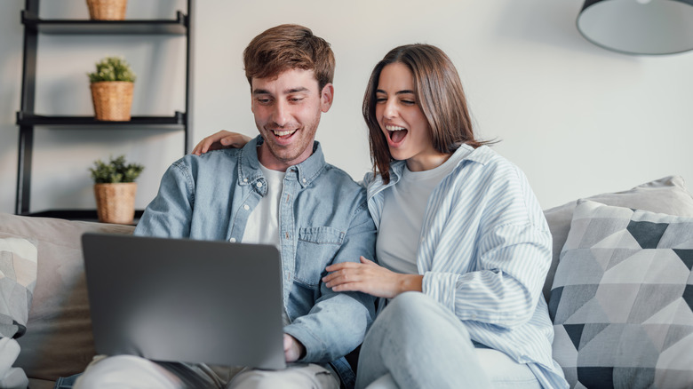 A happy couple receiving good news and smiling excitedly at a laptop