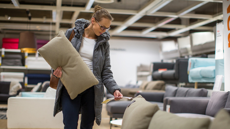 Woman holding green couch pillow and looking at price of couch